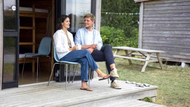 Couple sitting and talking in front of a cottage at Tunø Tent Site in Destination Coastal Land