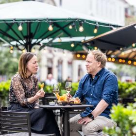 A man and a woman are sitting outside at a bar table under a green parasol